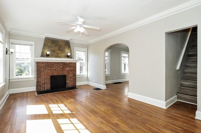 unfurnished living room featuring baseboards, arched walkways, wood finished floors, stairs, and crown molding