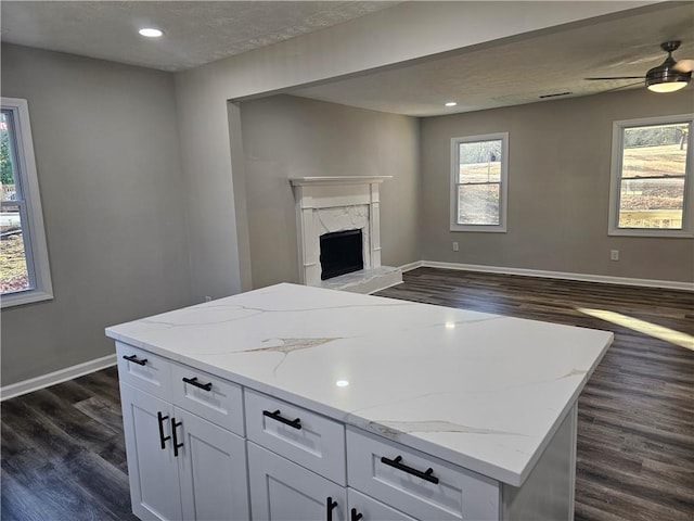 kitchen with dark wood-type flooring, a wealth of natural light, light stone countertops, and white cabinets