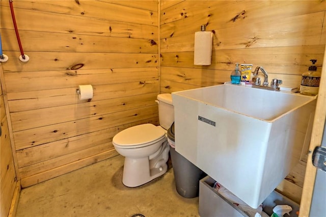 bathroom featuring toilet, sink, and wooden walls