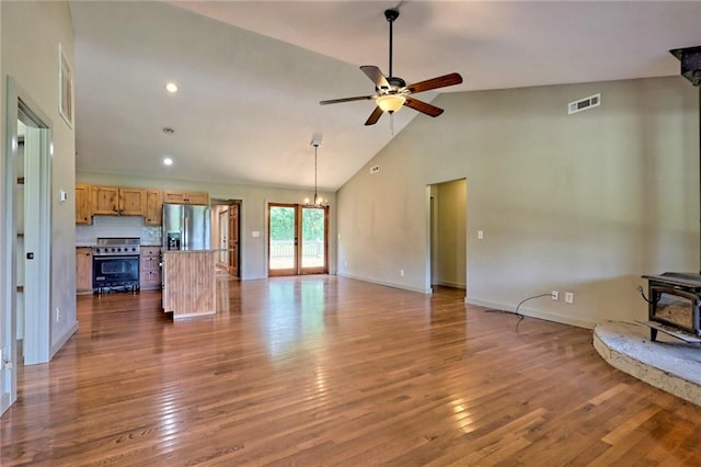 unfurnished living room featuring a wood stove, ceiling fan with notable chandelier, dark hardwood / wood-style floors, and high vaulted ceiling