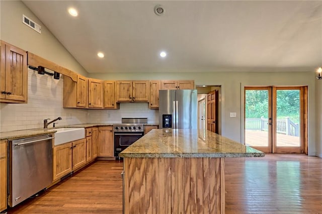 kitchen featuring a center island, sink, vaulted ceiling, light stone counters, and stainless steel appliances