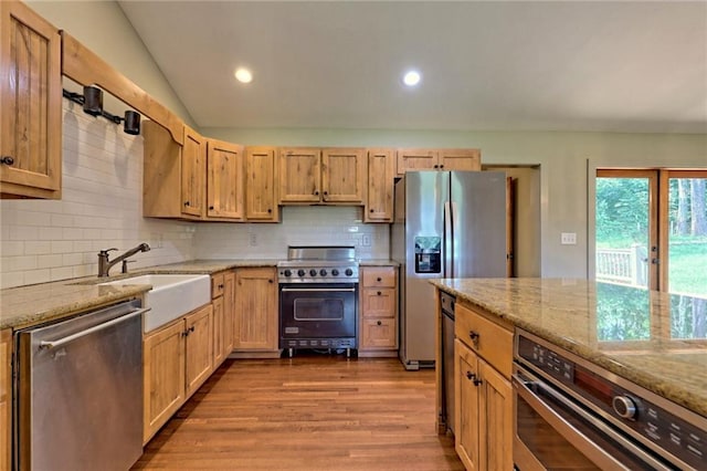 kitchen with light stone countertops, sink, light hardwood / wood-style flooring, lofted ceiling, and appliances with stainless steel finishes