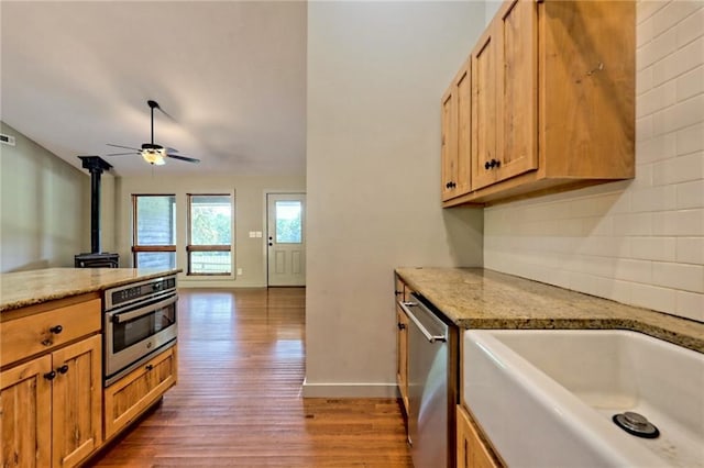 kitchen with hardwood / wood-style floors, a wood stove, sink, ceiling fan, and stainless steel appliances