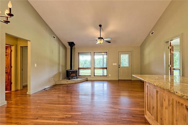 unfurnished living room with ceiling fan, dark hardwood / wood-style flooring, a wood stove, and vaulted ceiling