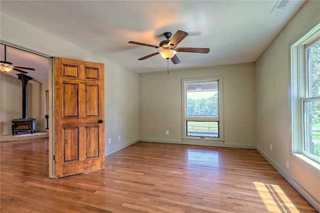 spare room featuring a wood stove, a wealth of natural light, ceiling fan, and light wood-type flooring