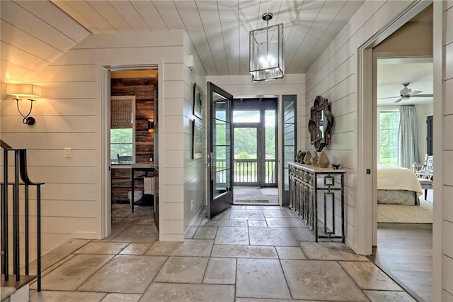 entrance foyer with ceiling fan with notable chandelier, wooden ceiling, vaulted ceiling, and wooden walls