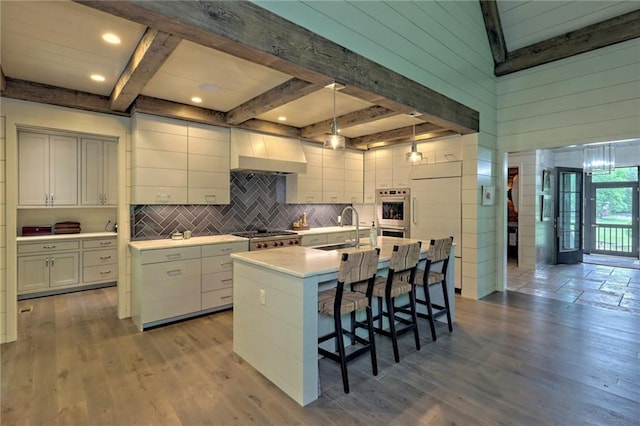 kitchen with sink, beamed ceiling, decorative light fixtures, a center island with sink, and custom range hood