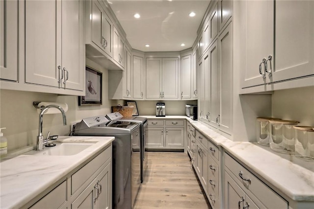 washroom with separate washer and dryer, sink, cabinets, and light hardwood / wood-style flooring