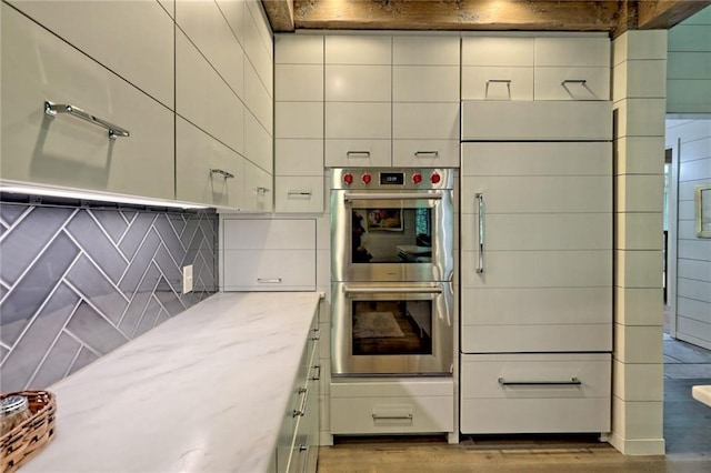 kitchen with double oven, decorative backsplash, light stone countertops, and light hardwood / wood-style floors