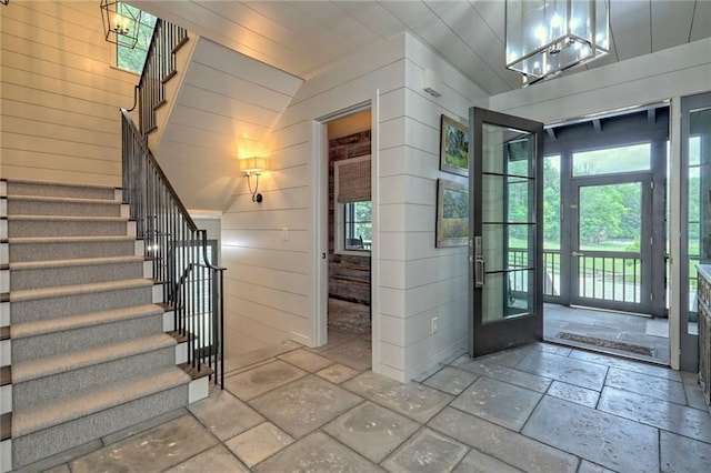 entrance foyer featuring wooden walls, a chandelier, and vaulted ceiling