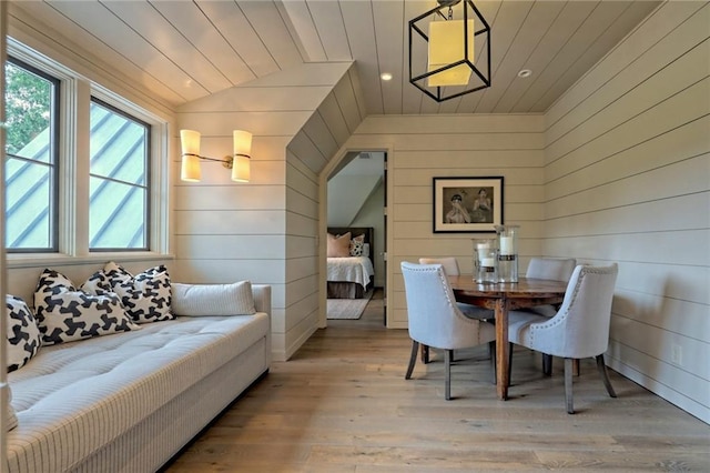 dining space featuring light wood-type flooring, wooden ceiling, wooden walls, and vaulted ceiling