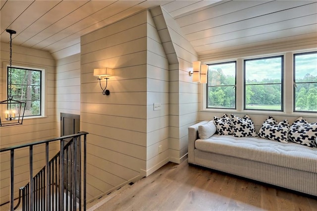 living area with wood walls, light wood-type flooring, lofted ceiling, and a wealth of natural light