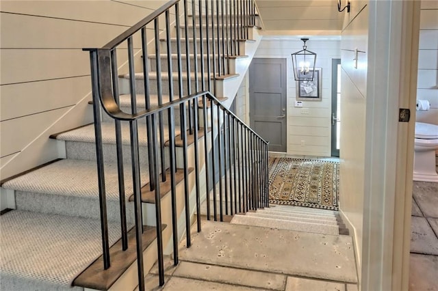 stairs with wood walls, an inviting chandelier, and concrete floors