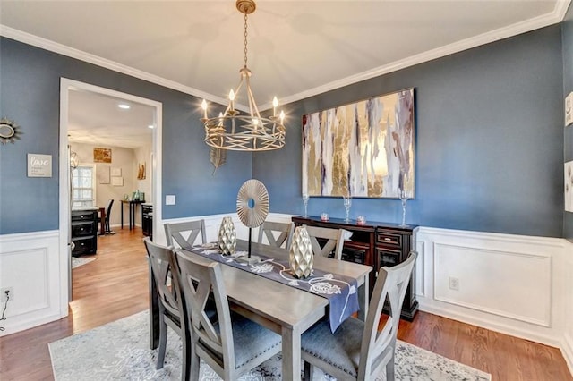 dining area with a notable chandelier, ornamental molding, wood finished floors, and wainscoting