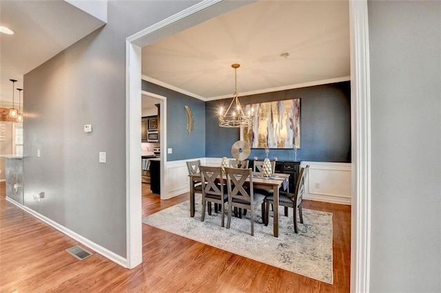 dining room with crown molding, visible vents, wainscoting, wood finished floors, and a chandelier