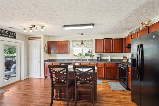 kitchen featuring decorative light fixtures, black appliances, dark wood-type flooring, and a kitchen bar