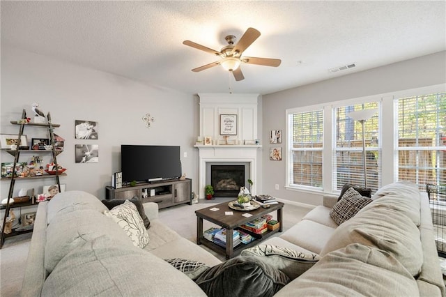 living room with a textured ceiling, ceiling fan, a fireplace, and light carpet