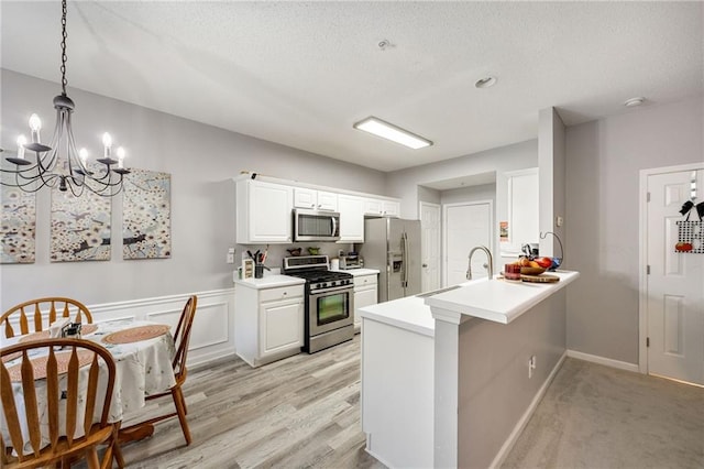 kitchen with kitchen peninsula, appliances with stainless steel finishes, white cabinets, a chandelier, and hanging light fixtures