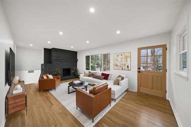 living area featuring light wood finished floors, a brick fireplace, baseboards, and recessed lighting