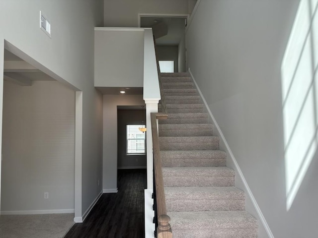 stairs featuring a towering ceiling, wood finished floors, visible vents, and baseboards