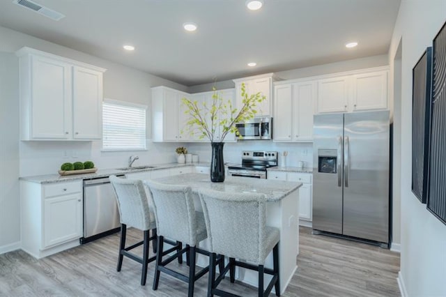 kitchen featuring a breakfast bar, stainless steel appliances, sink, white cabinets, and a kitchen island