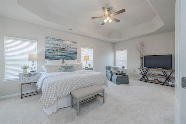 bedroom with light colored carpet, a raised ceiling, and ceiling fan