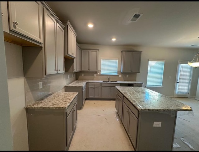 kitchen featuring gray cabinets, light stone countertops, sink, and a kitchen island