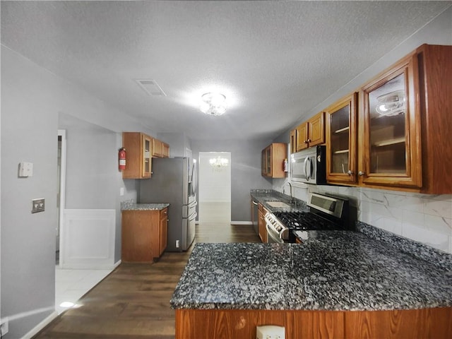 kitchen featuring sink, dark hardwood / wood-style floors, a textured ceiling, appliances with stainless steel finishes, and kitchen peninsula