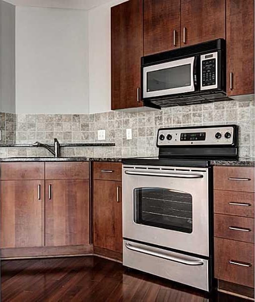 kitchen featuring dark wood-type flooring, sink, decorative backsplash, dark stone countertops, and stainless steel appliances