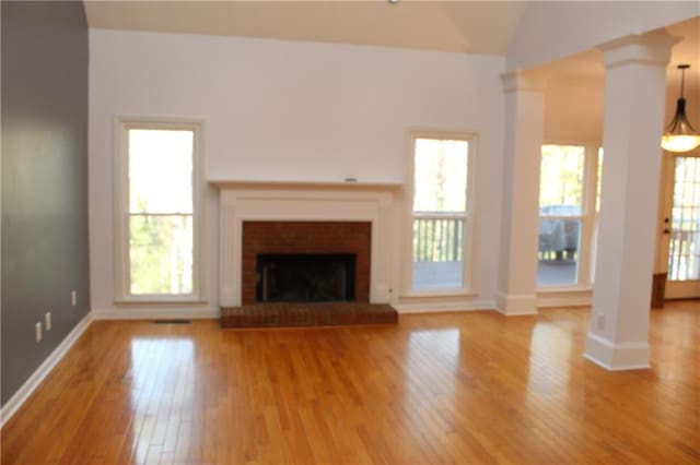 unfurnished living room with a brick fireplace, ornate columns, vaulted ceiling, and hardwood / wood-style flooring