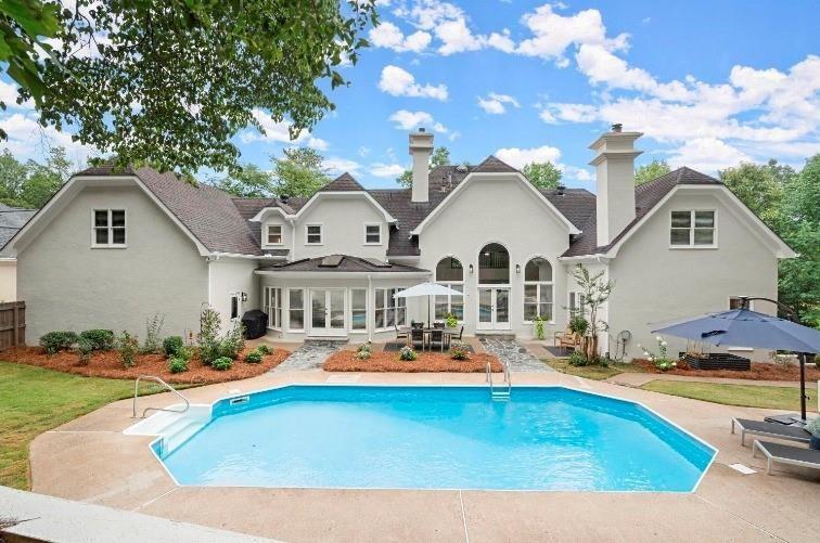 rear view of property with stucco siding, an outdoor pool, a patio, and french doors