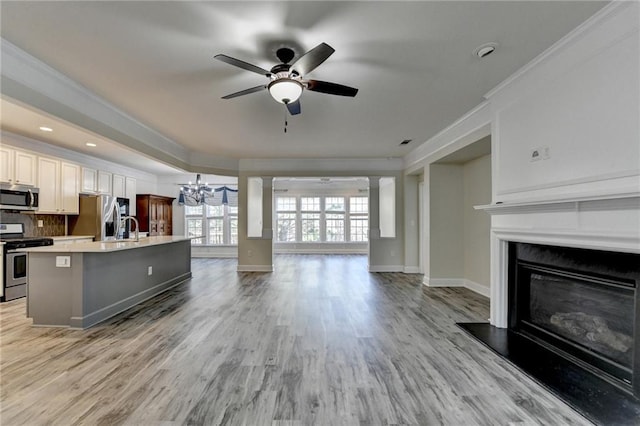 kitchen with light countertops, appliances with stainless steel finishes, ornamental molding, open floor plan, and a kitchen island with sink