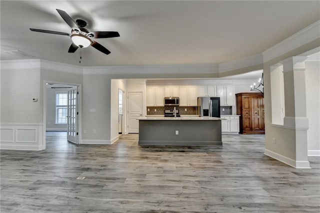 kitchen with open floor plan, stainless steel appliances, ornamental molding, and an island with sink