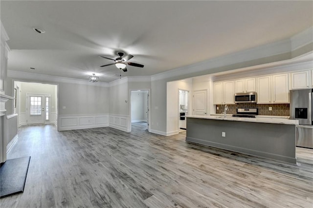 kitchen featuring open floor plan, stainless steel appliances, light countertops, light wood-type flooring, and a sink