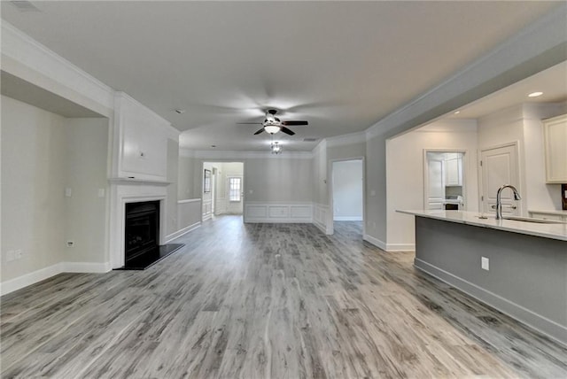 unfurnished living room with a fireplace with raised hearth, light wood finished floors, a sink, and crown molding