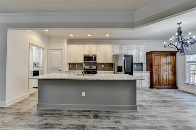 kitchen with a kitchen island with sink, a sink, light countertops, appliances with stainless steel finishes, and crown molding