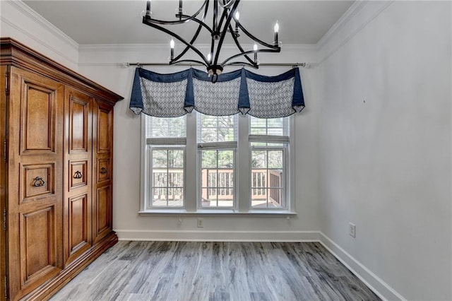 unfurnished dining area featuring baseboards, ornamental molding, a chandelier, and wood finished floors