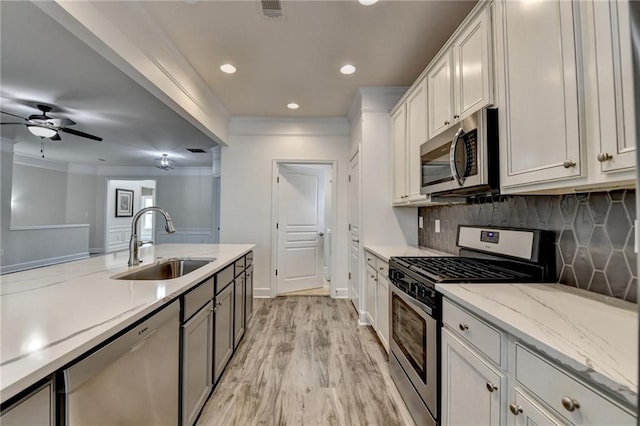 kitchen featuring crown molding, light wood finished floors, tasteful backsplash, appliances with stainless steel finishes, and a sink