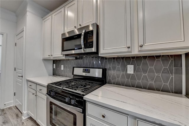 kitchen with stainless steel appliances, white cabinets, light stone countertops, light wood finished floors, and tasteful backsplash