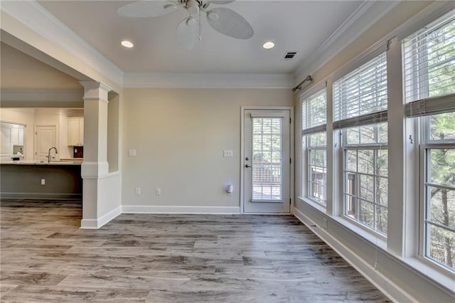 interior space featuring baseboards, ornamental molding, wood finished floors, ornate columns, and a sink