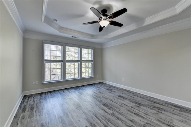 empty room with baseboards, crown molding, a tray ceiling, and wood finished floors