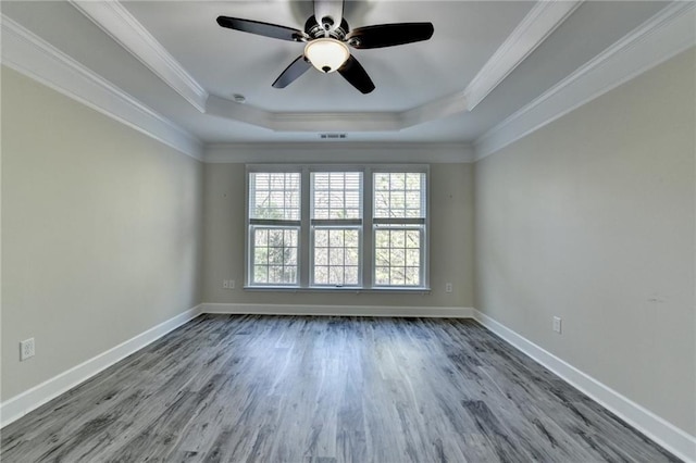 empty room with a tray ceiling, wood finished floors, and ornamental molding