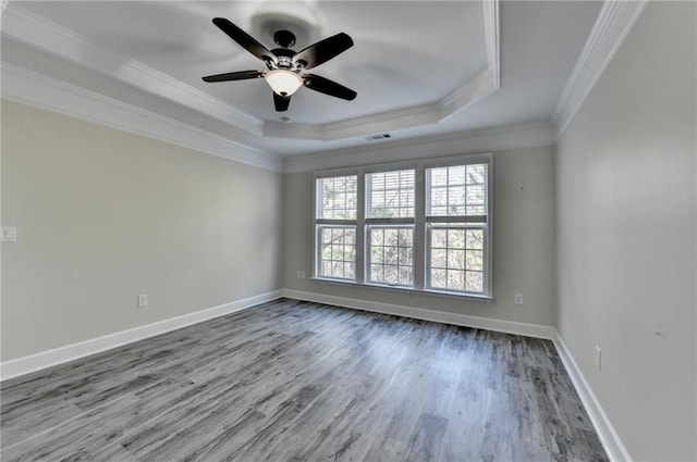 unfurnished room featuring baseboards, visible vents, a raised ceiling, ornamental molding, and wood finished floors