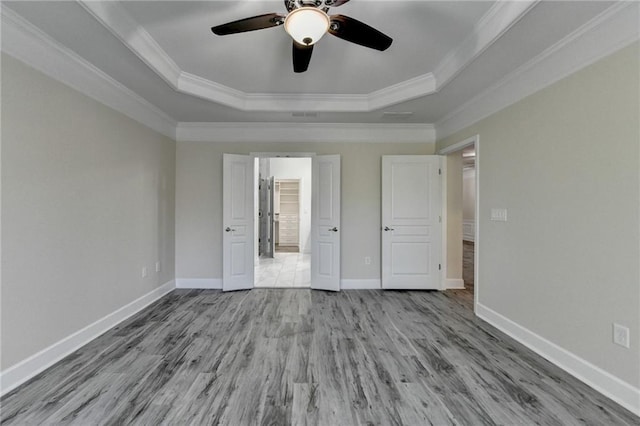 unfurnished bedroom featuring baseboards, crown molding, a tray ceiling, and wood finished floors