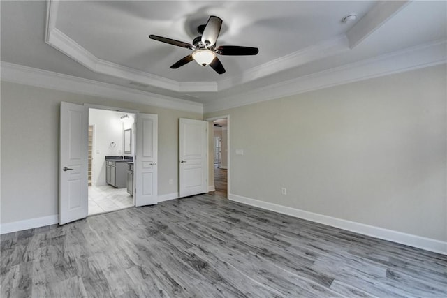 unfurnished bedroom featuring baseboards, a raised ceiling, ensuite bath, wood finished floors, and crown molding