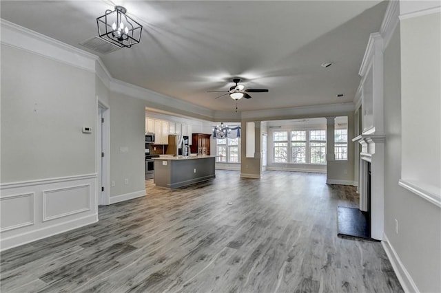 unfurnished living room featuring ceiling fan with notable chandelier, a fireplace with raised hearth, light wood-style flooring, and crown molding