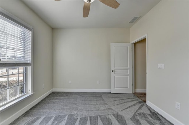 empty room featuring a ceiling fan, carpet, visible vents, and baseboards