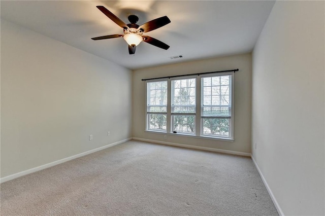 spare room with a ceiling fan, light colored carpet, visible vents, and baseboards