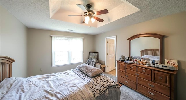 bedroom with light colored carpet, a textured ceiling, visible vents, and a raised ceiling