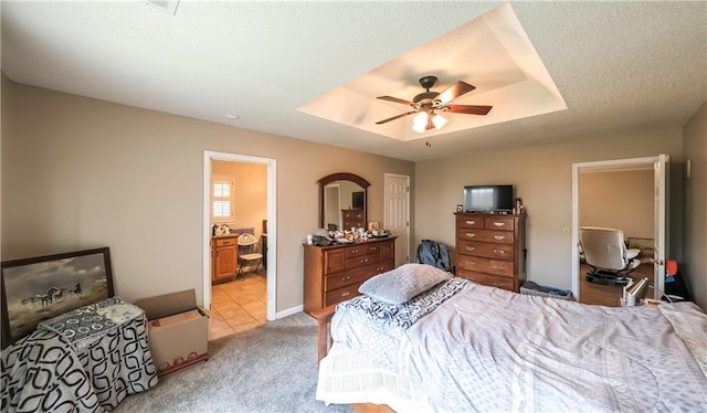 bedroom with connected bathroom, light carpet, a ceiling fan, and a raised ceiling